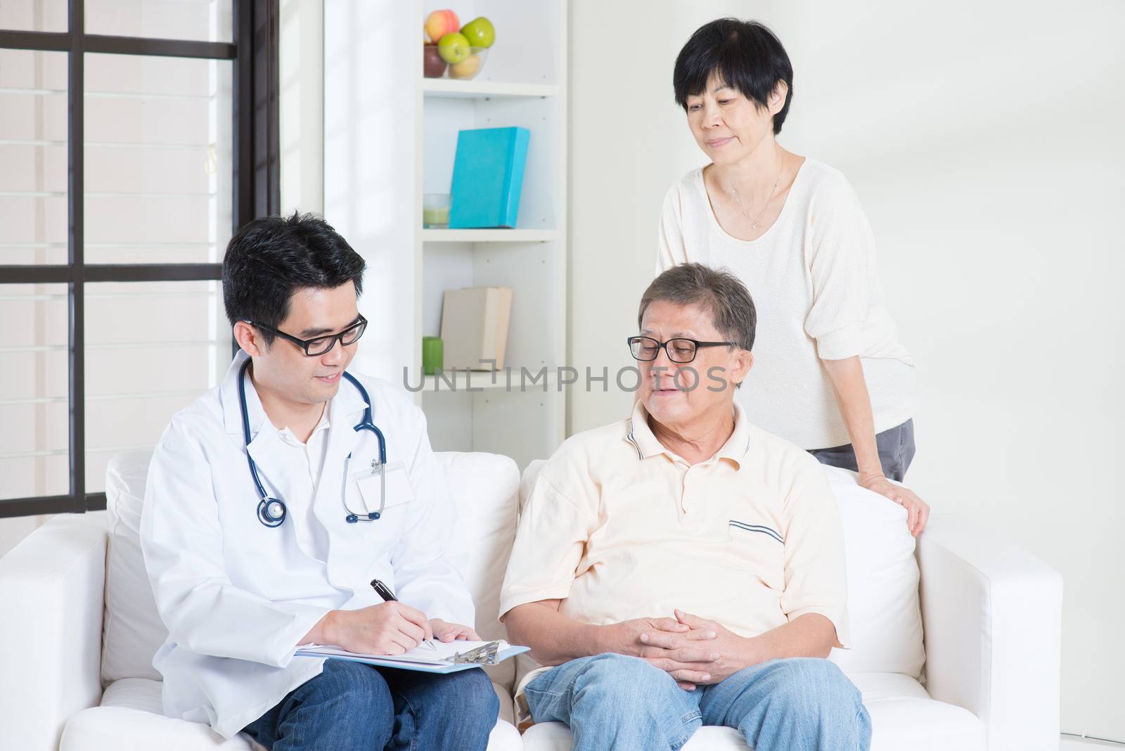 Doctor and patient. Asian senior couple consult family doctor, sitting on sofa. Senior retiree indoors living lifestyle.