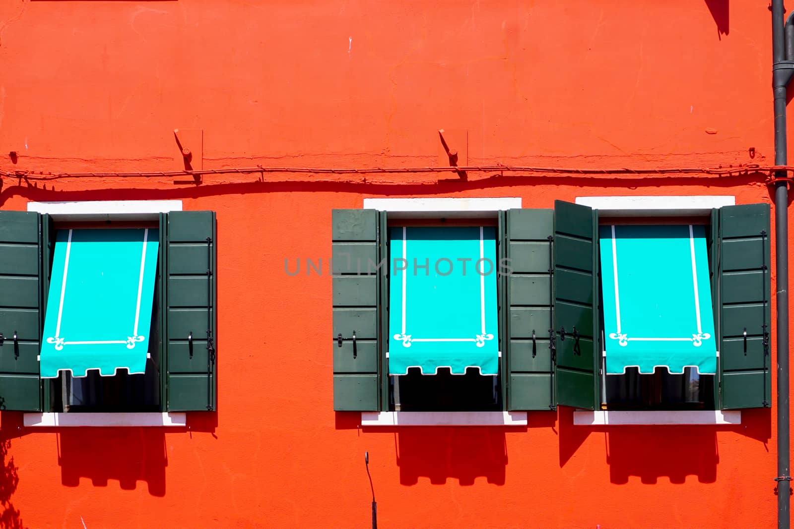 three Windows with blue canopy in Burano on red orange wall building architecture, Venice, Italy