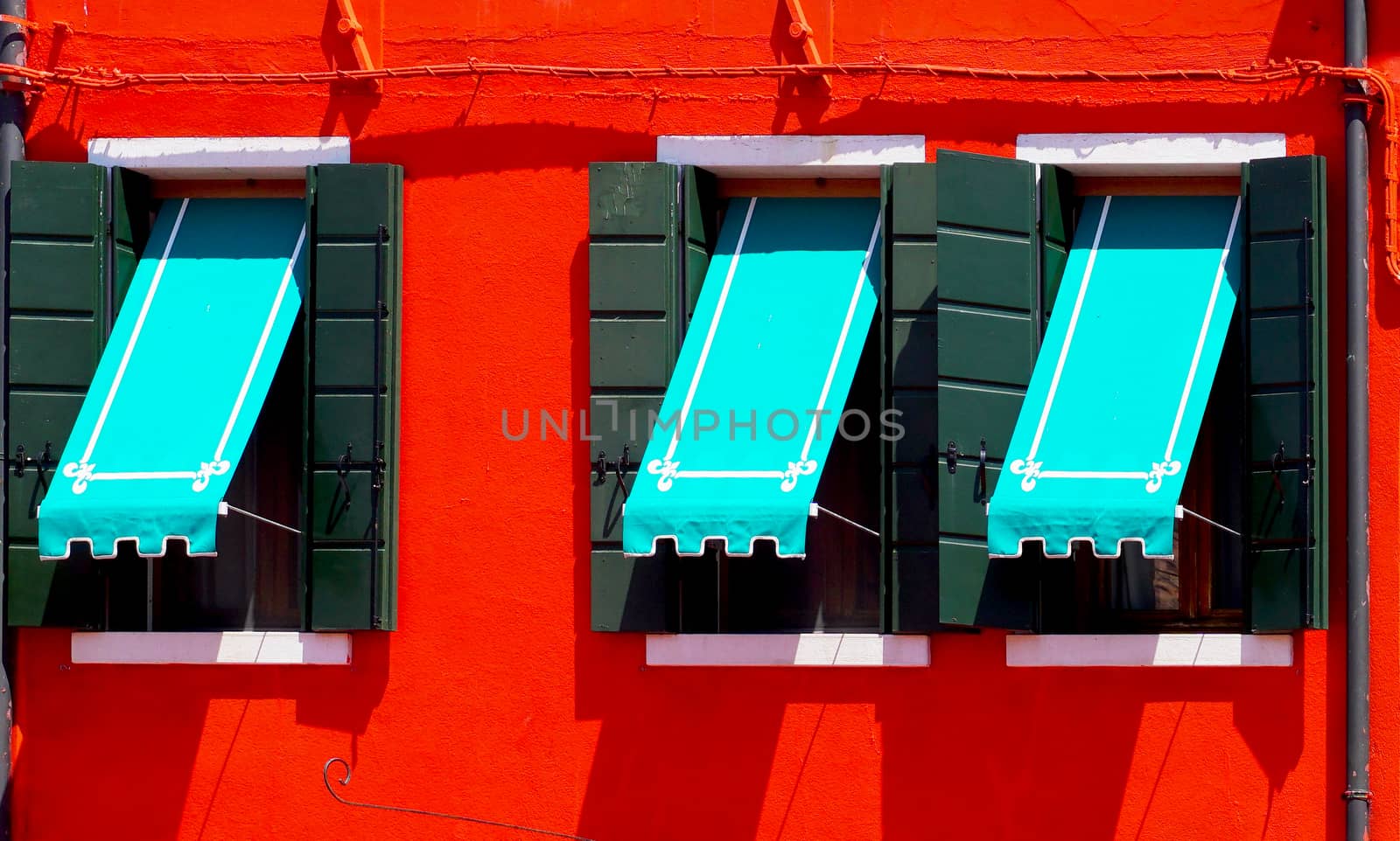 three Windows with blue canopy in Burano on red wall building architecture, Venice, Italy
