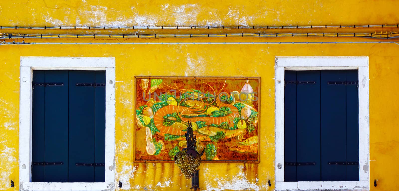 Two Windows with white frame in Burano on yellow color decay wall building architecture, Venice, Italy