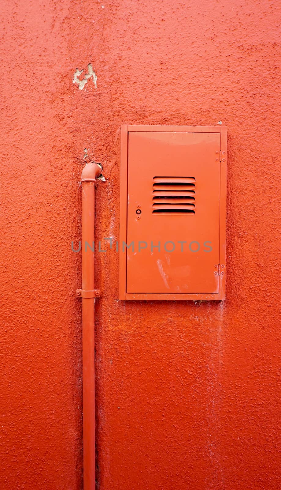 vertical metal pipe and electric box on orange color wall in Burano, Venice, Italy