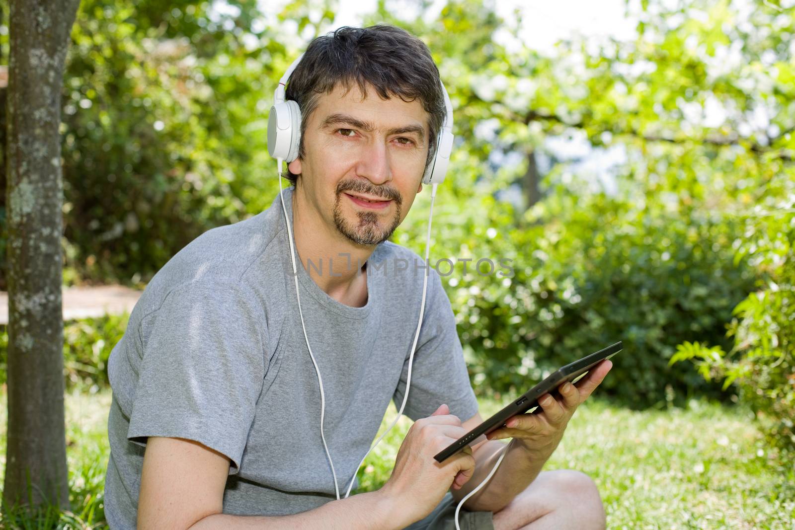 young man holding a tablet with headphones, outdoor