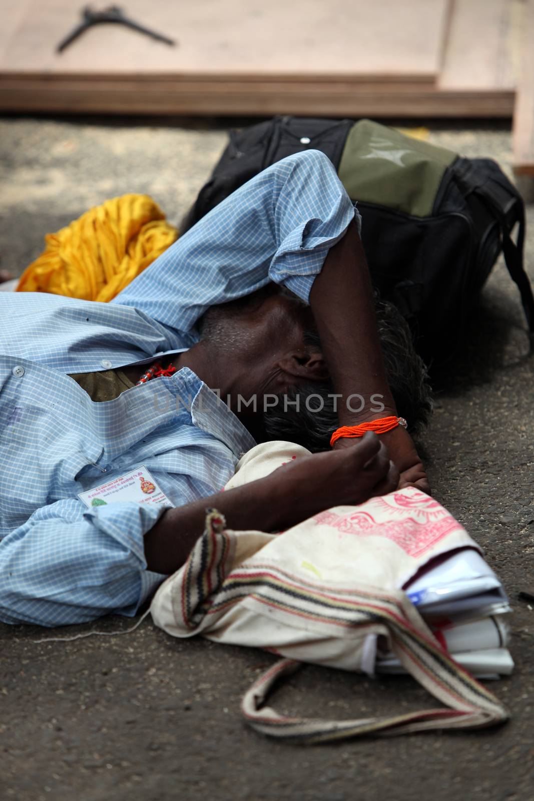 A poor tired man sleeps on the side of a road in India.