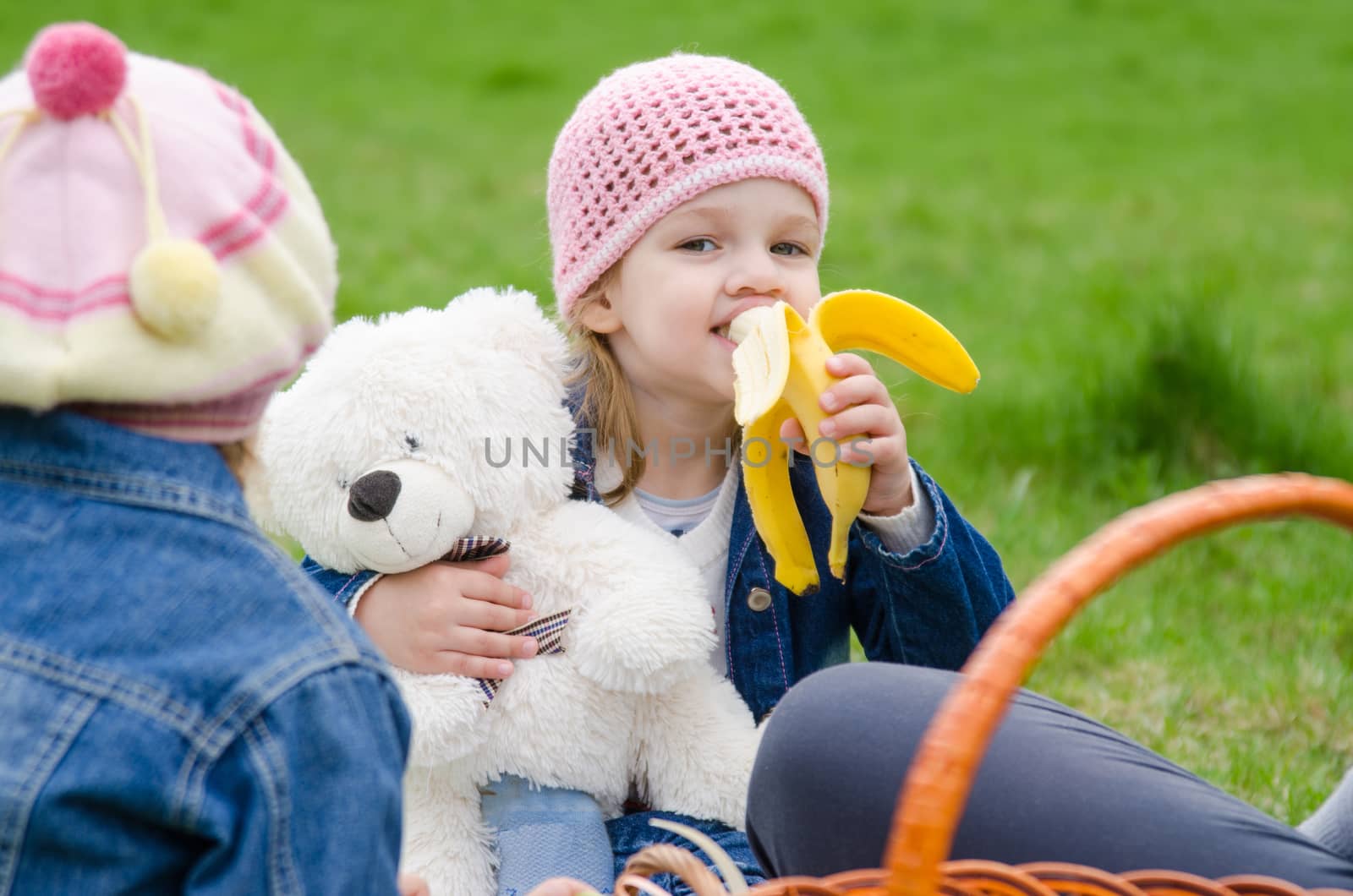 Girl on picnic eats a banana and holds bear by Madhourse