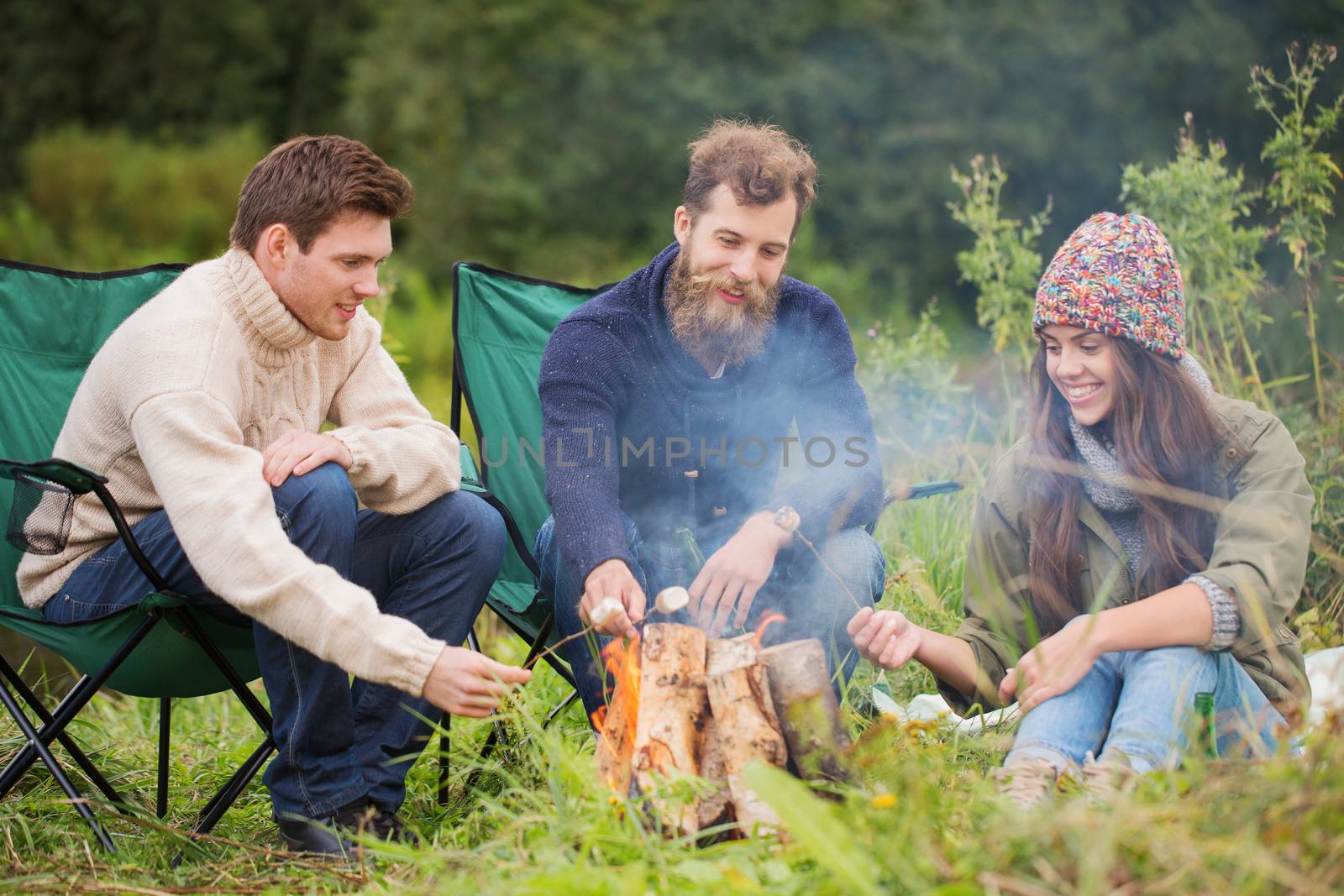group of smiling friends sitting around bonfire by dolgachov