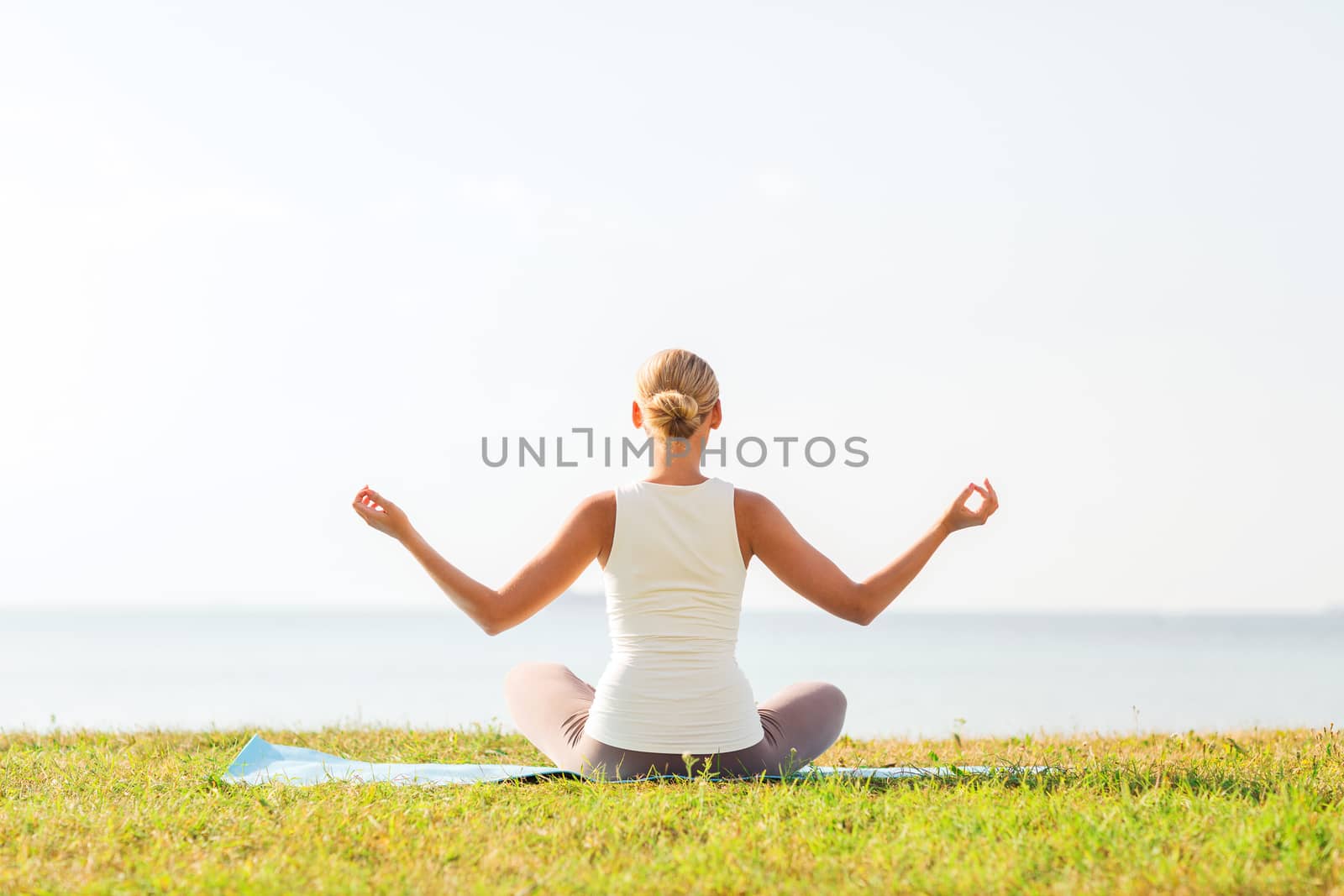 fitness, sport, people and lifestyle concept - of woman making yoga exercises on mat outdoors from back