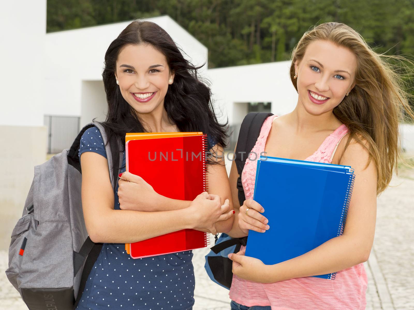 Two beautiful teenage students holding backpacks and smiling