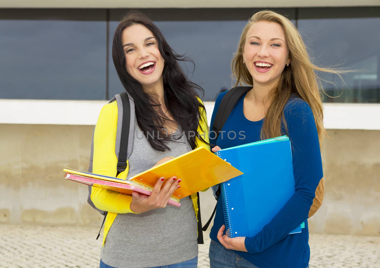 Two beautiful and happy teenage students showing something on the books