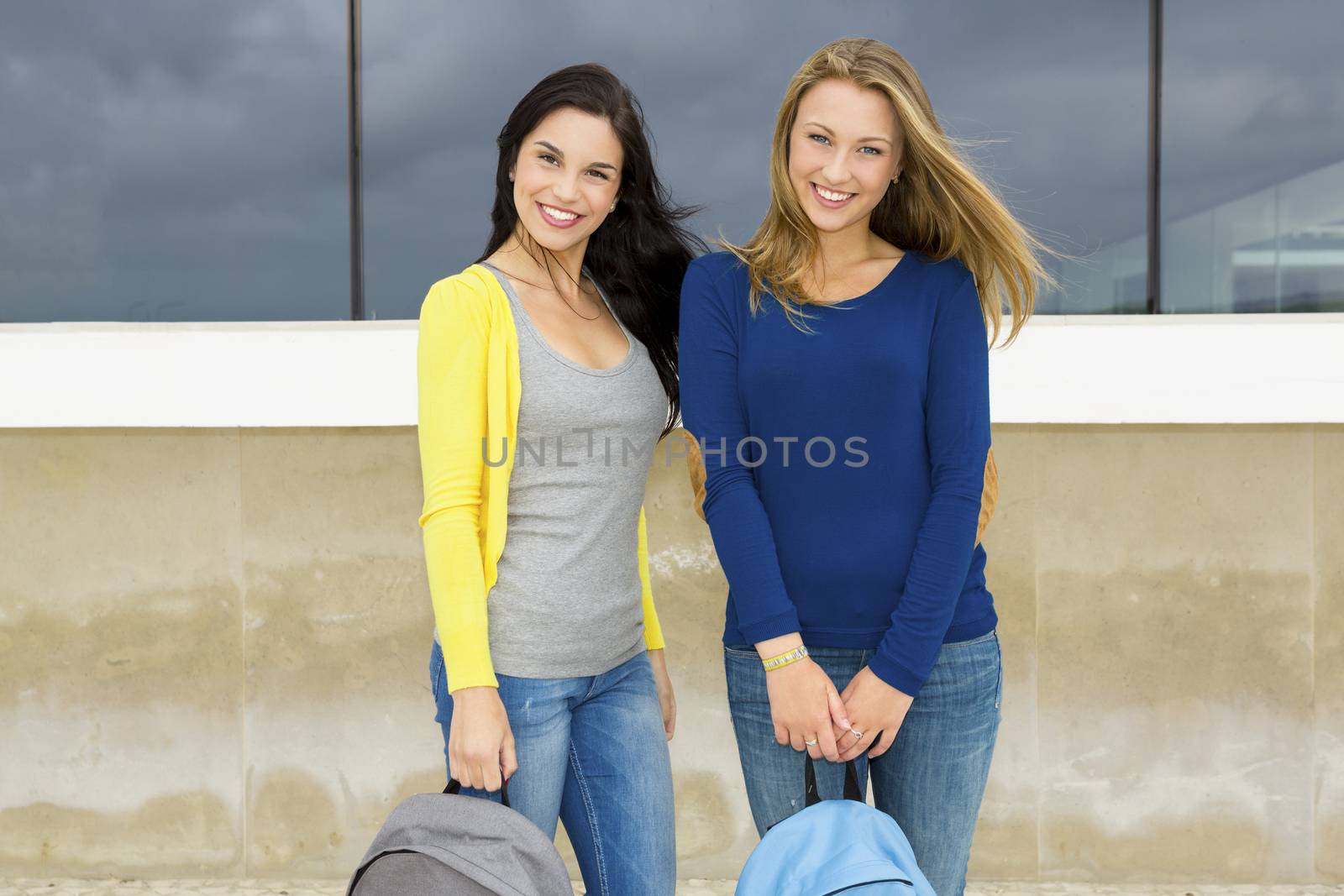 Two beautiful teenage students holding backpacks and smiling