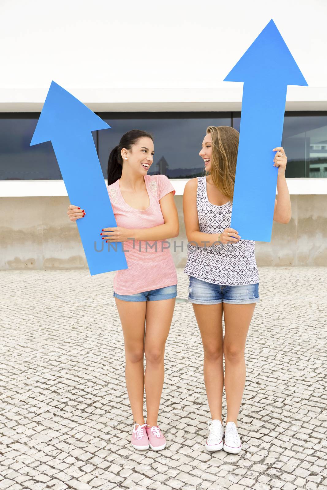 Two beautiful and happy girls holding a giant blue arrow 