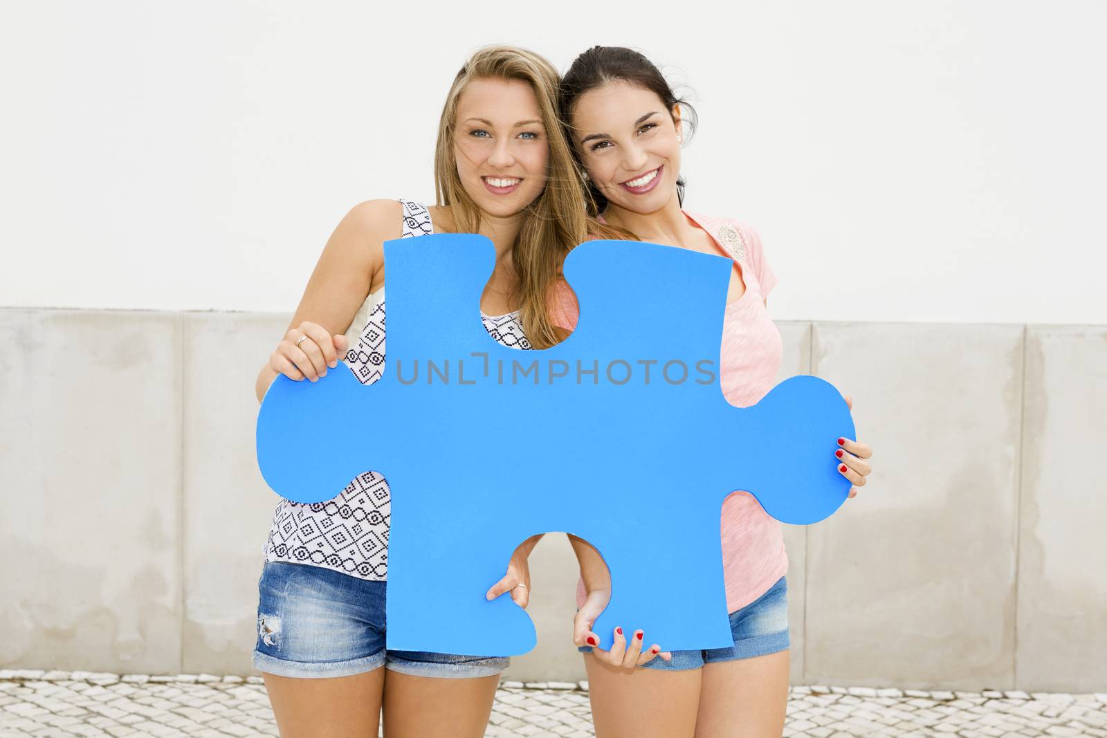 Two happy girls holding a giant puzzle piece 