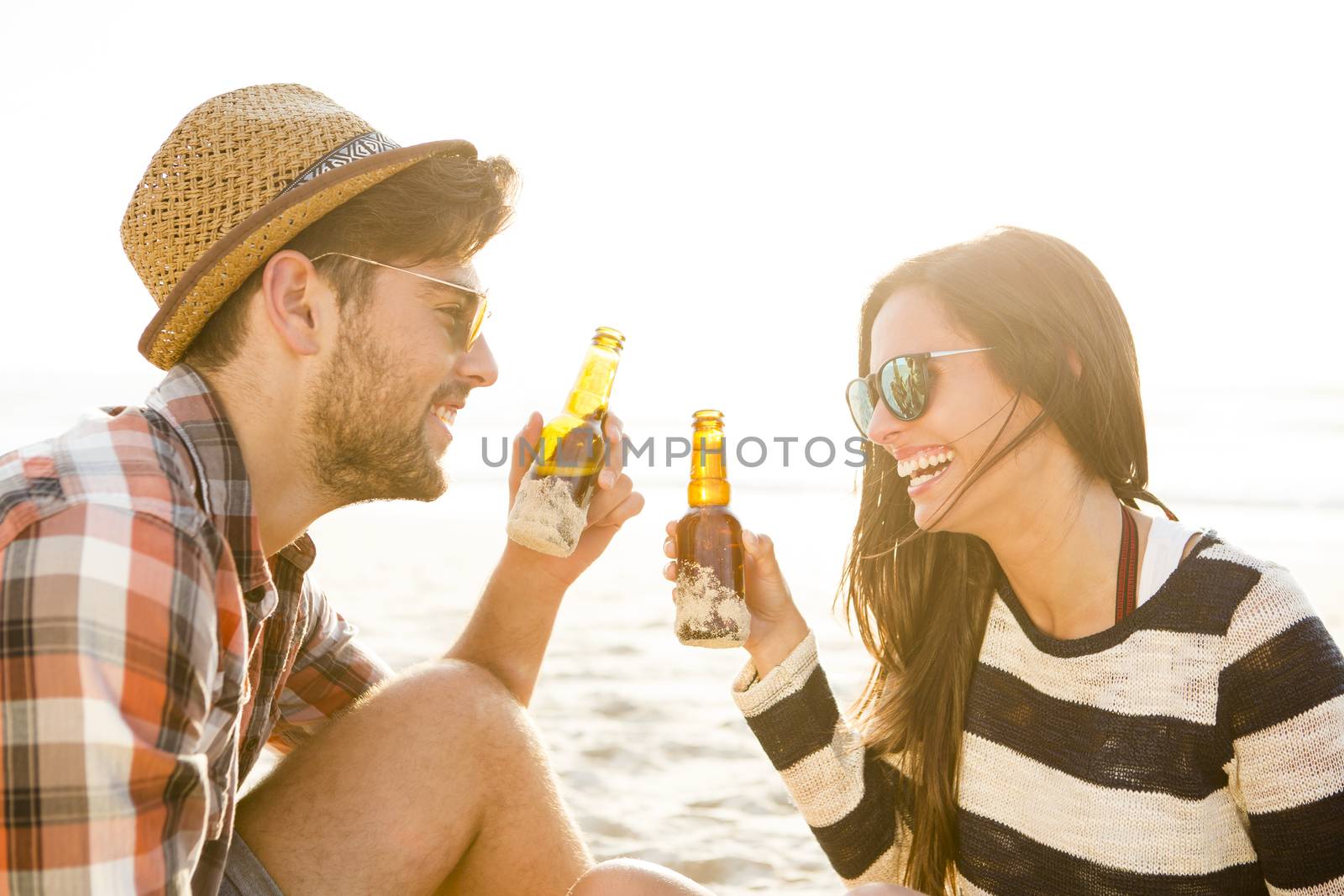 Young couple at the beach having fun, laughing and drinking beer