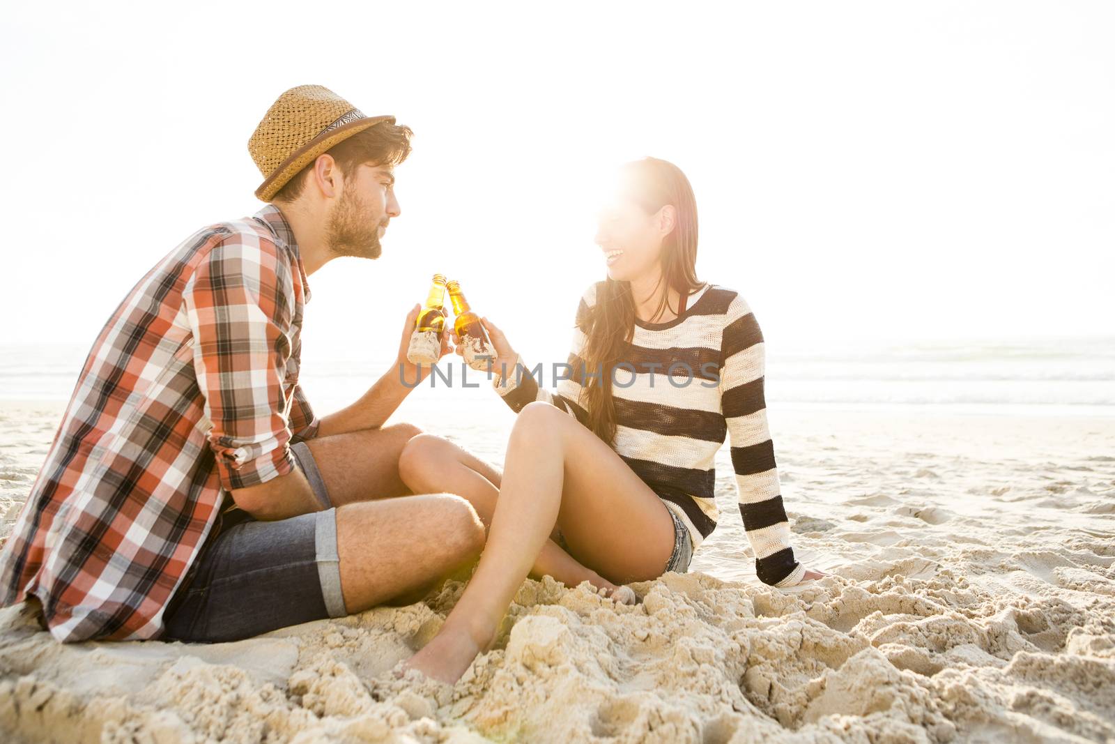 Young couple at the beach having fun, laughing and drinking beer