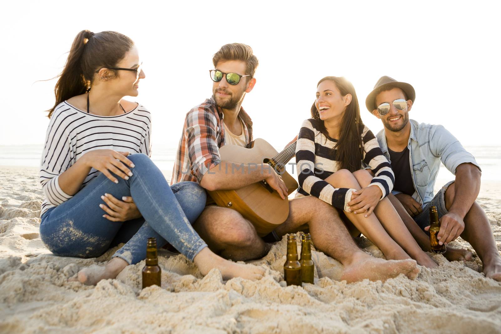 Friends having fun together at the beach, playing guitar and drinking beer