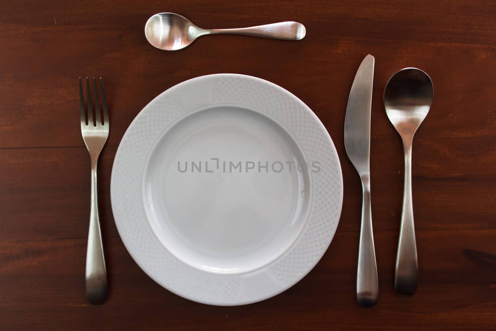 empty white plate with cutlery over wooden table