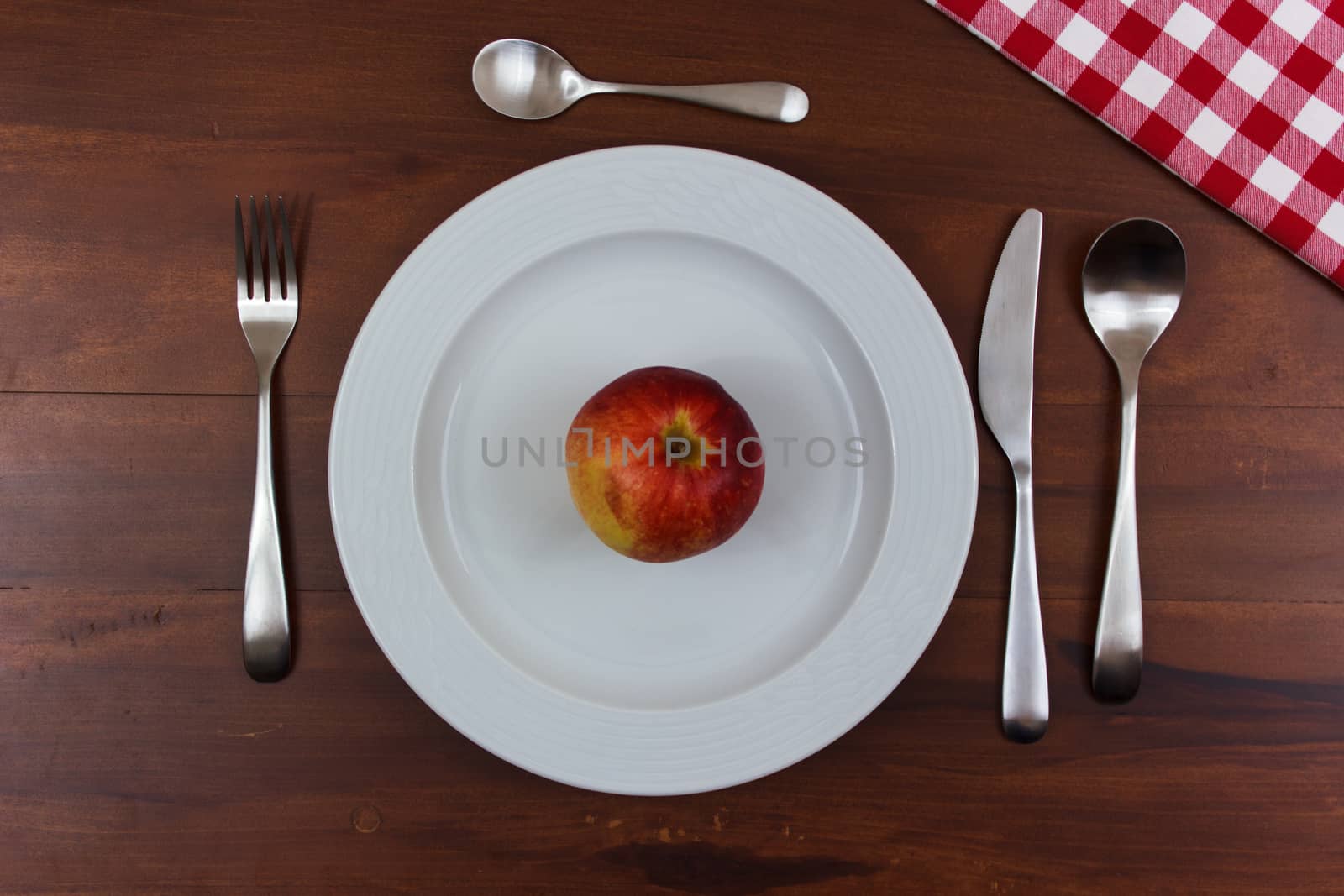 white dish with cutlery and apple in the center of wooden table
