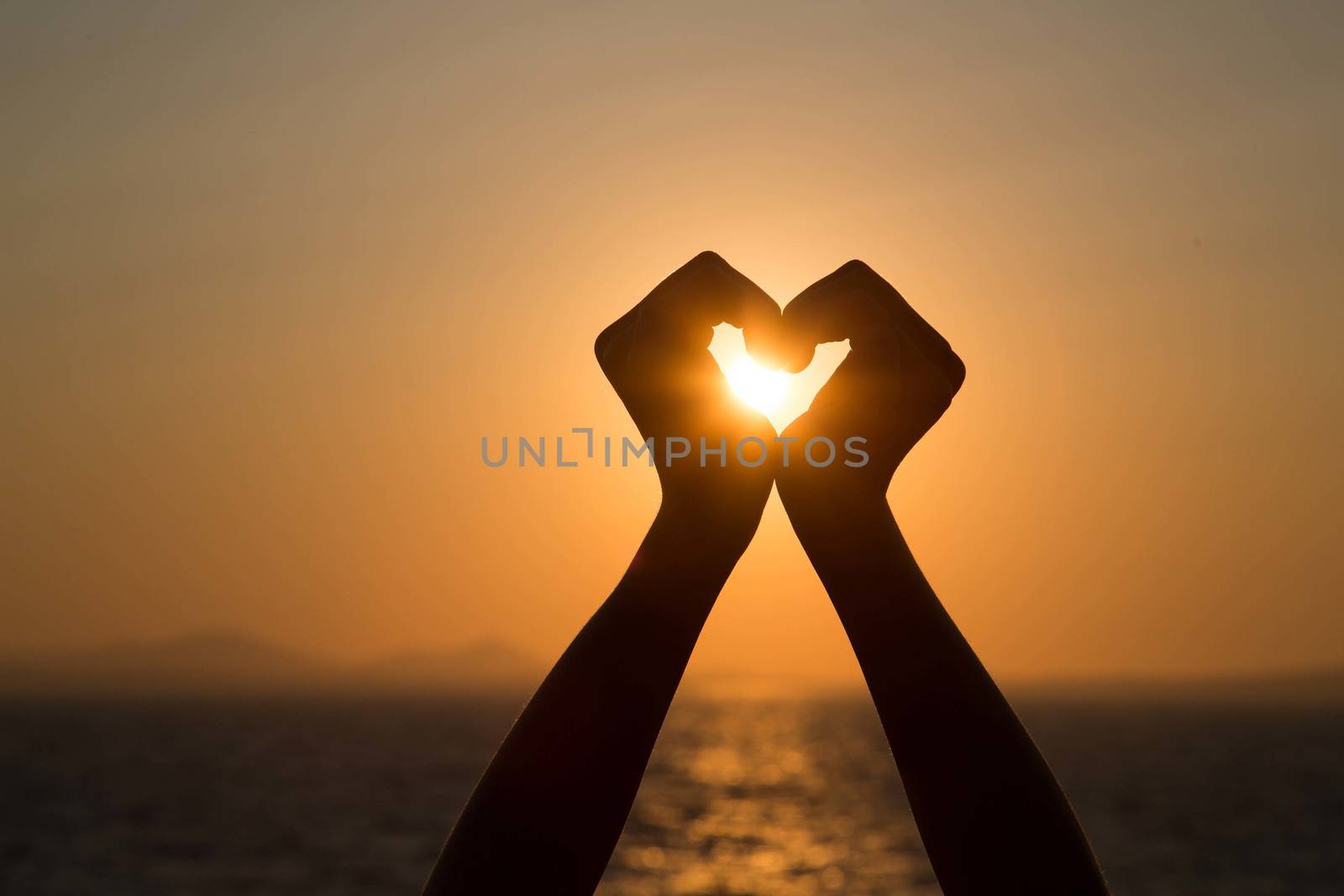 Silhouettes hand heart shaped with sun sets and the sky orange