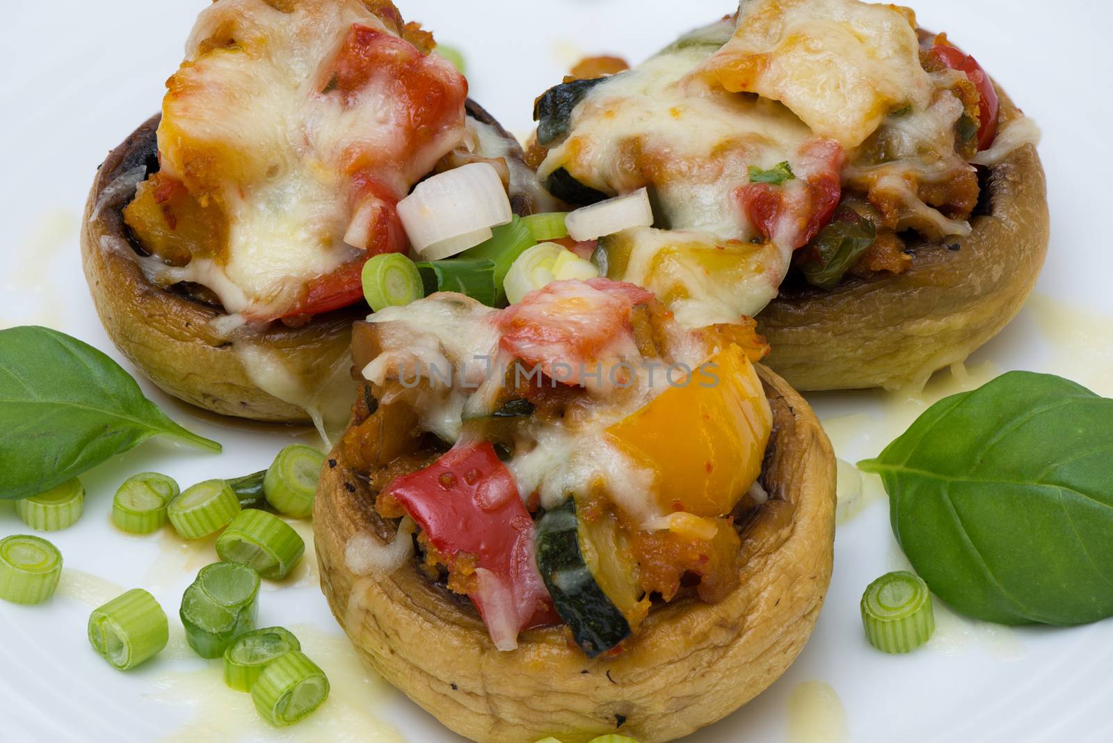 Mushrooms stuffed with vegetables and cheese on white plate fork and knife