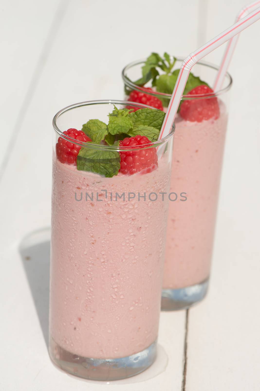 Fresh homemade raspberry smoothie in a glass, served outside in a garden on a white wood table