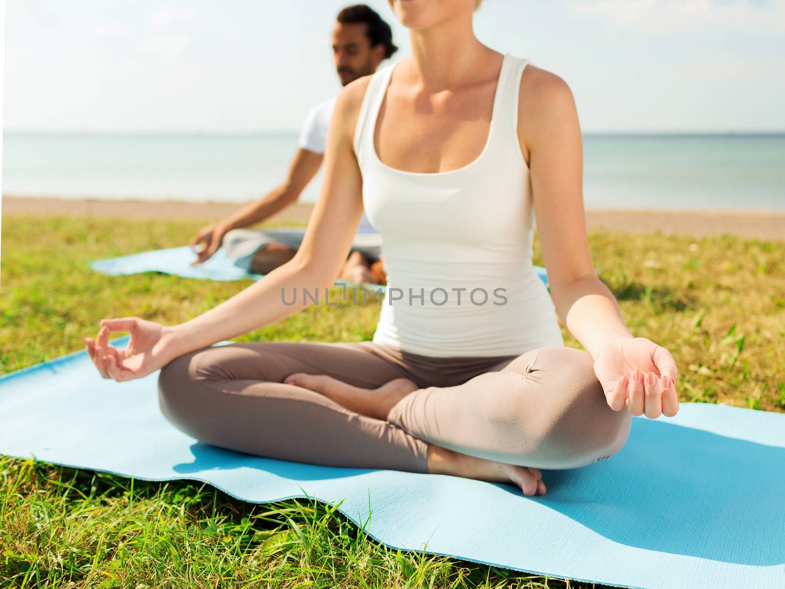 fitness, sport, people and lifestyle concept - close up of couple making yoga exercises sitting on mats outdoors