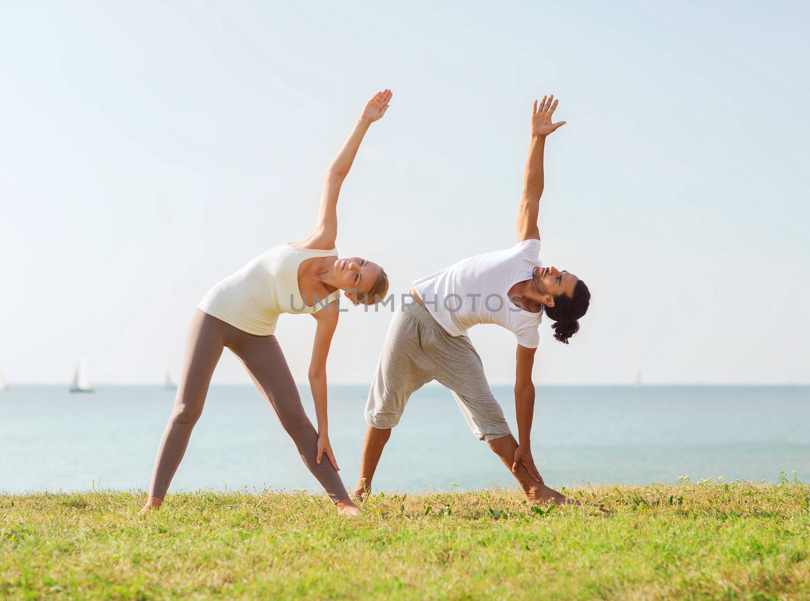 couple making yoga exercises outdoors by dolgachov