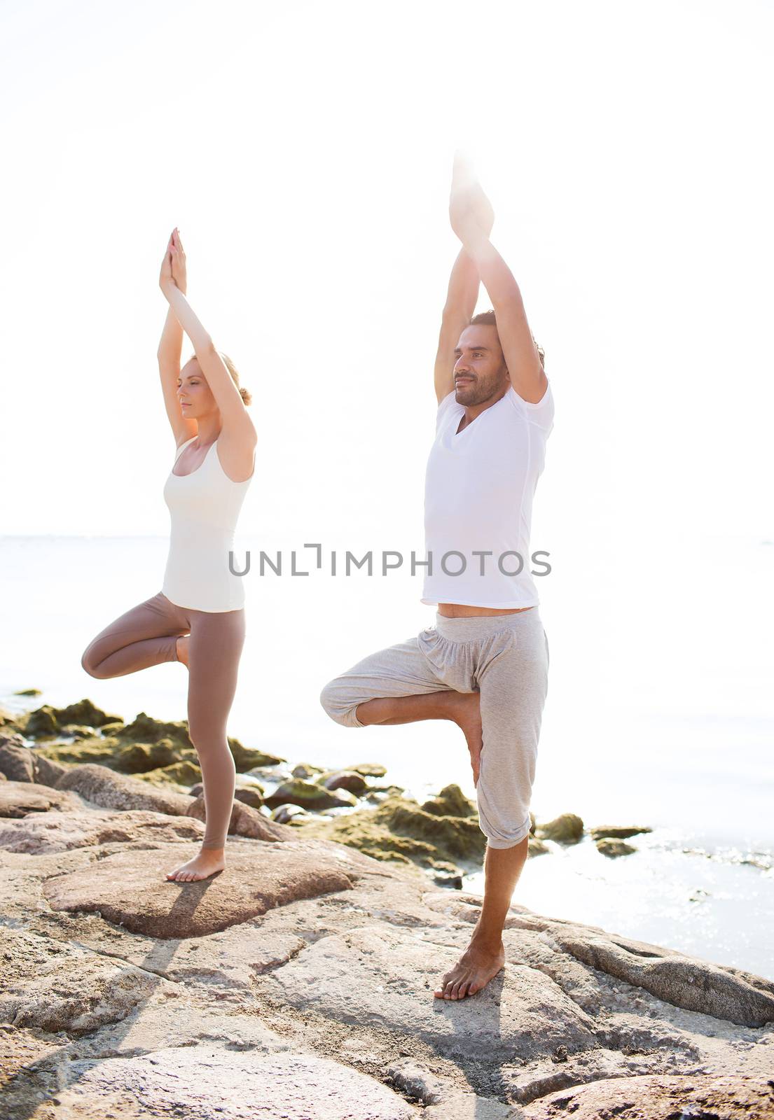 fitness, sport, friendship and lifestyle concept - couple making yoga exercises on beach