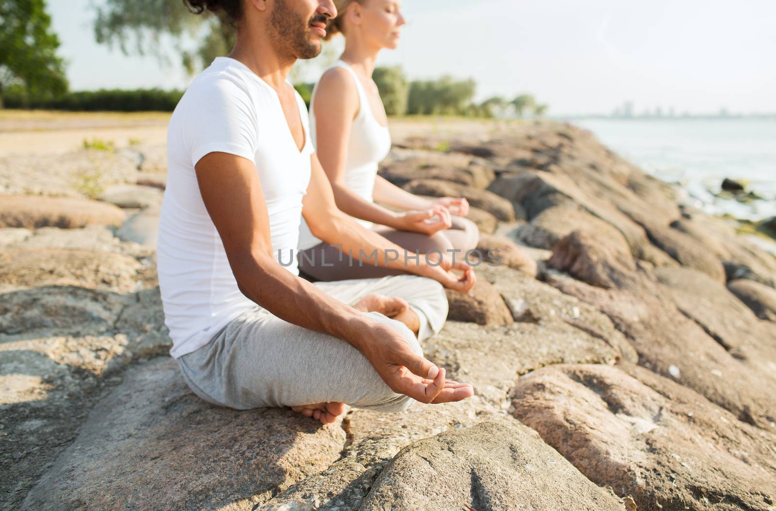 close up of couple making yoga exercises outdoors by dolgachov