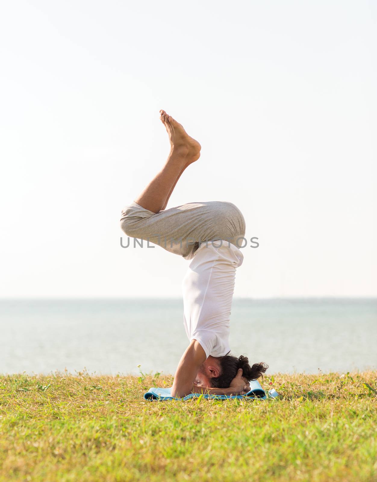 fitness, sport, people and lifestyle concept - man making yoga exercises on sand outdoors