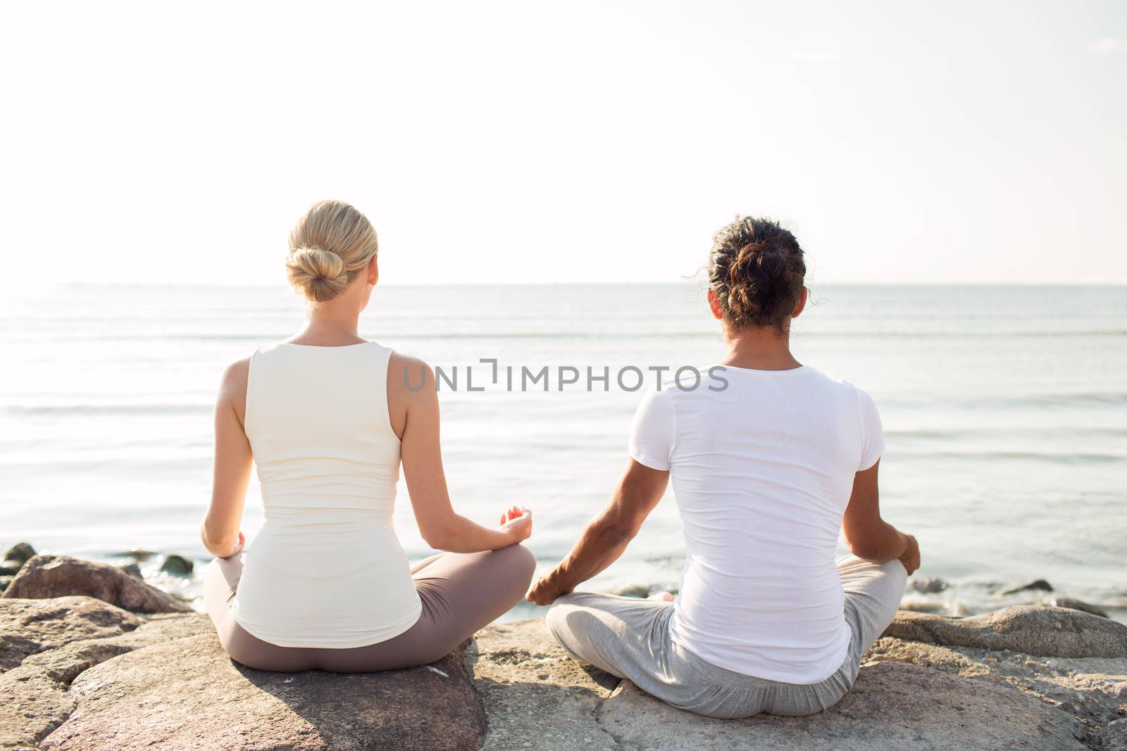 fitness, sport, people and lifestyle concept - couple making yoga exercises sitting on pier outdoors from back