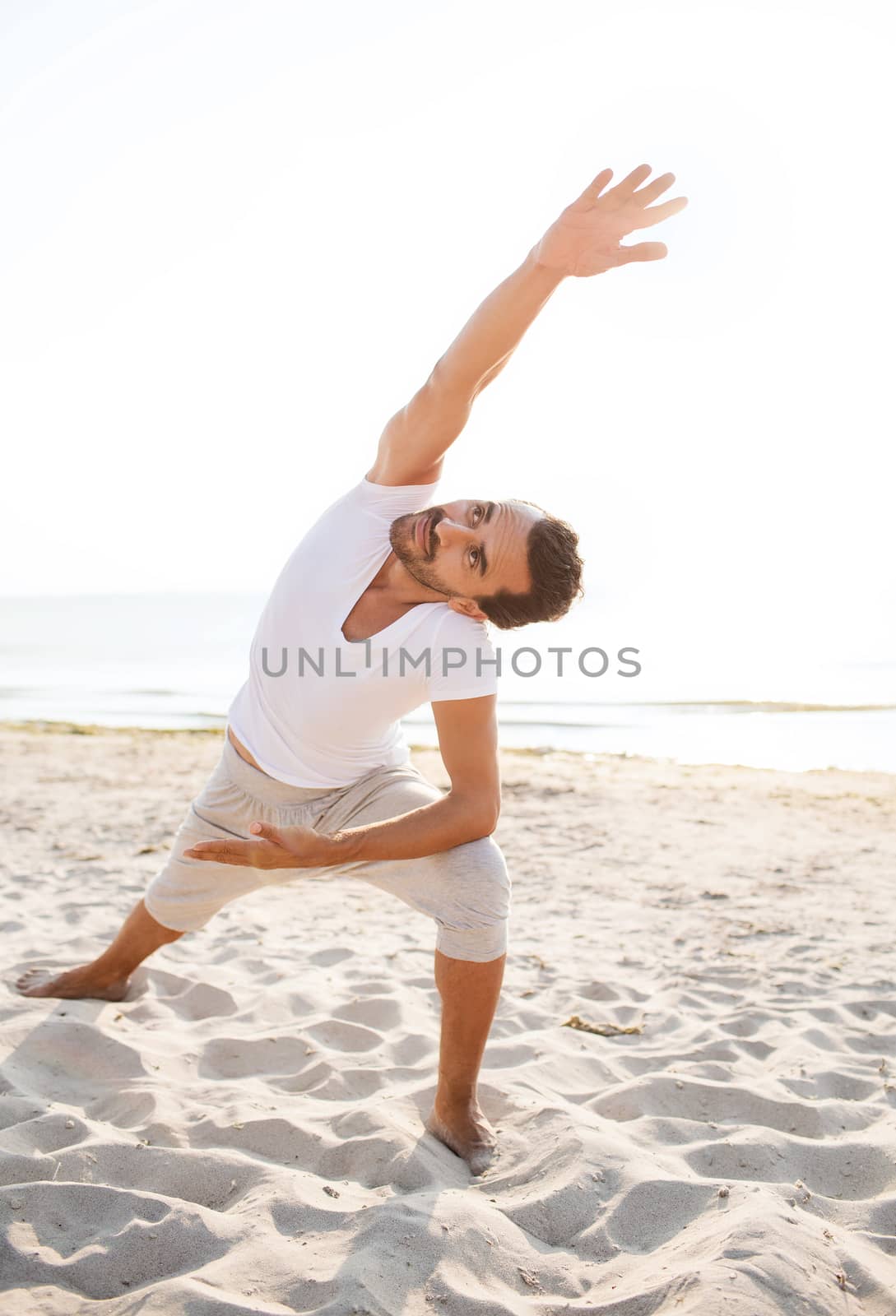 smiling man making yoga exercises outdoors by dolgachov