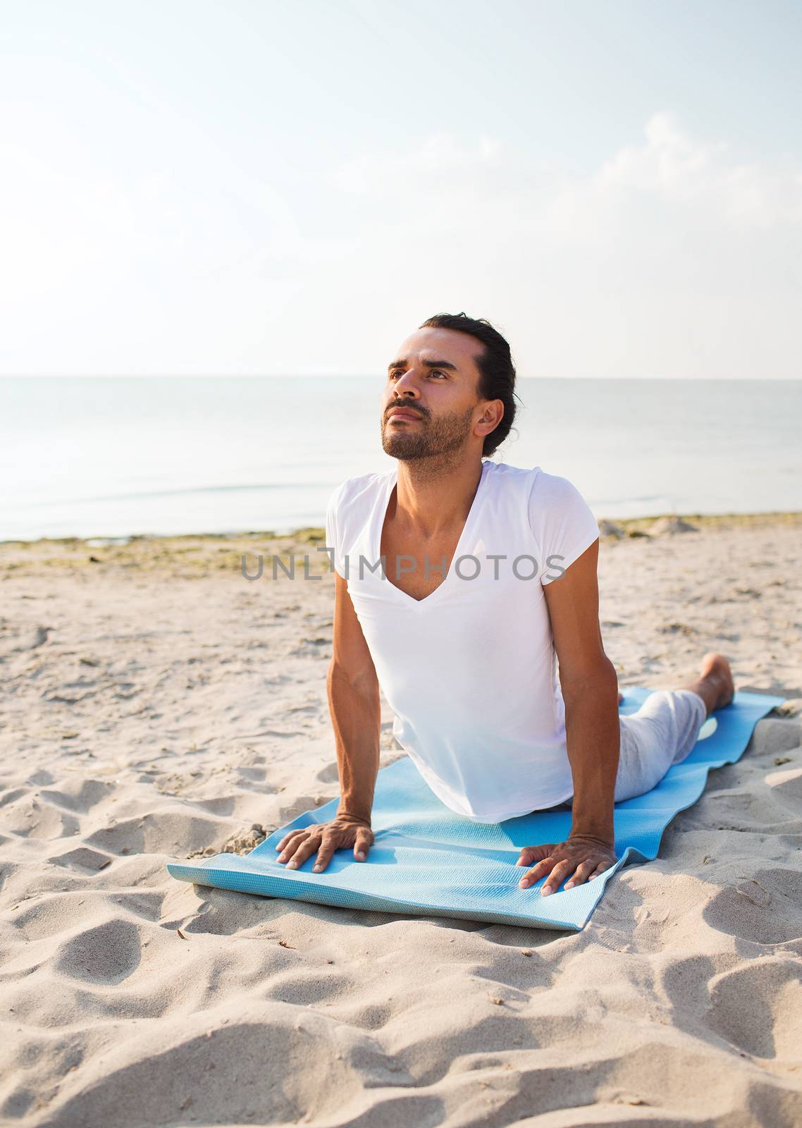 fitness, sport and lifestyle concept - man doing yoga exercises lying on mat outdoors