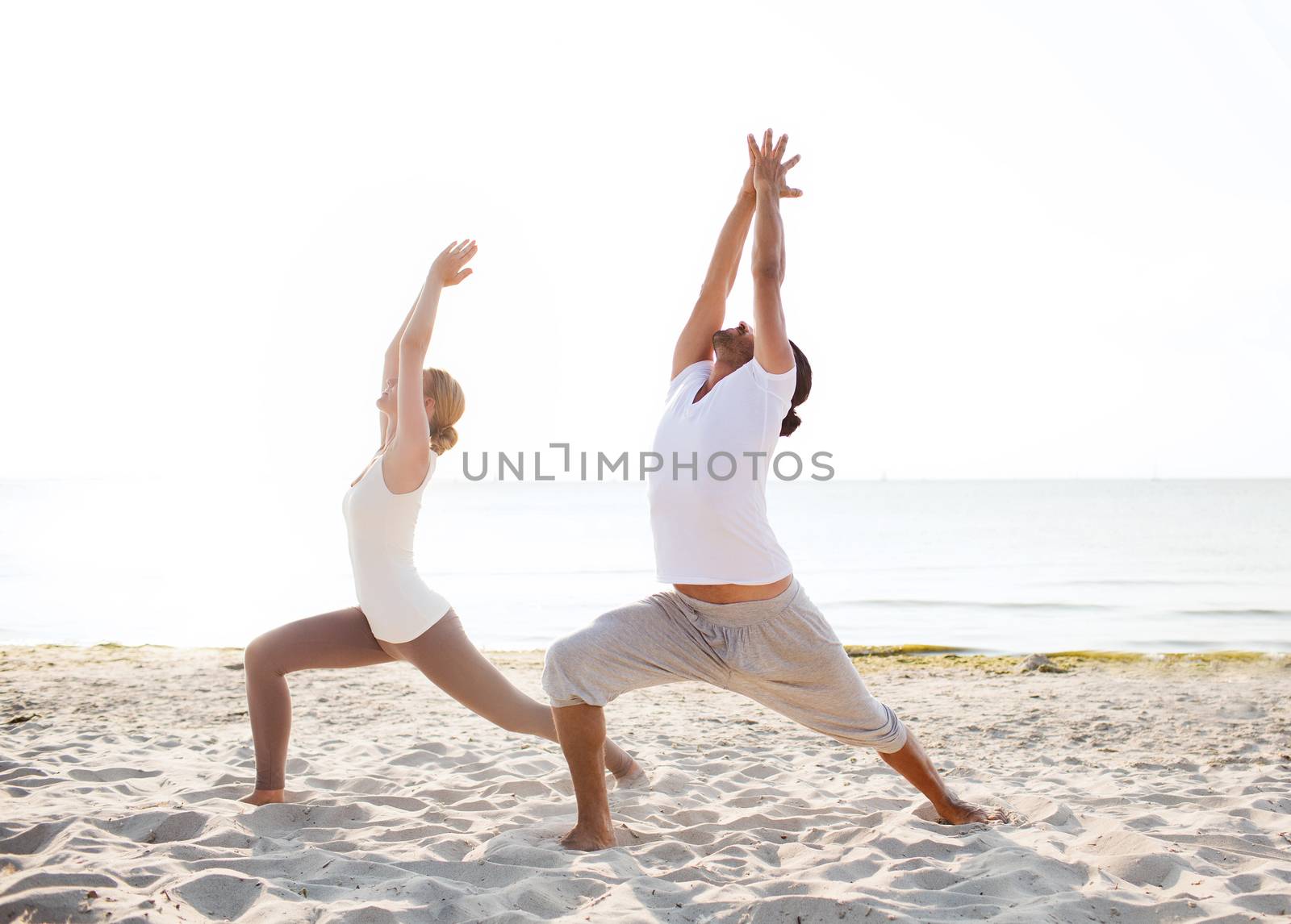 fitness, sport, friendship and lifestyle concept - couple making yoga exercises on beach