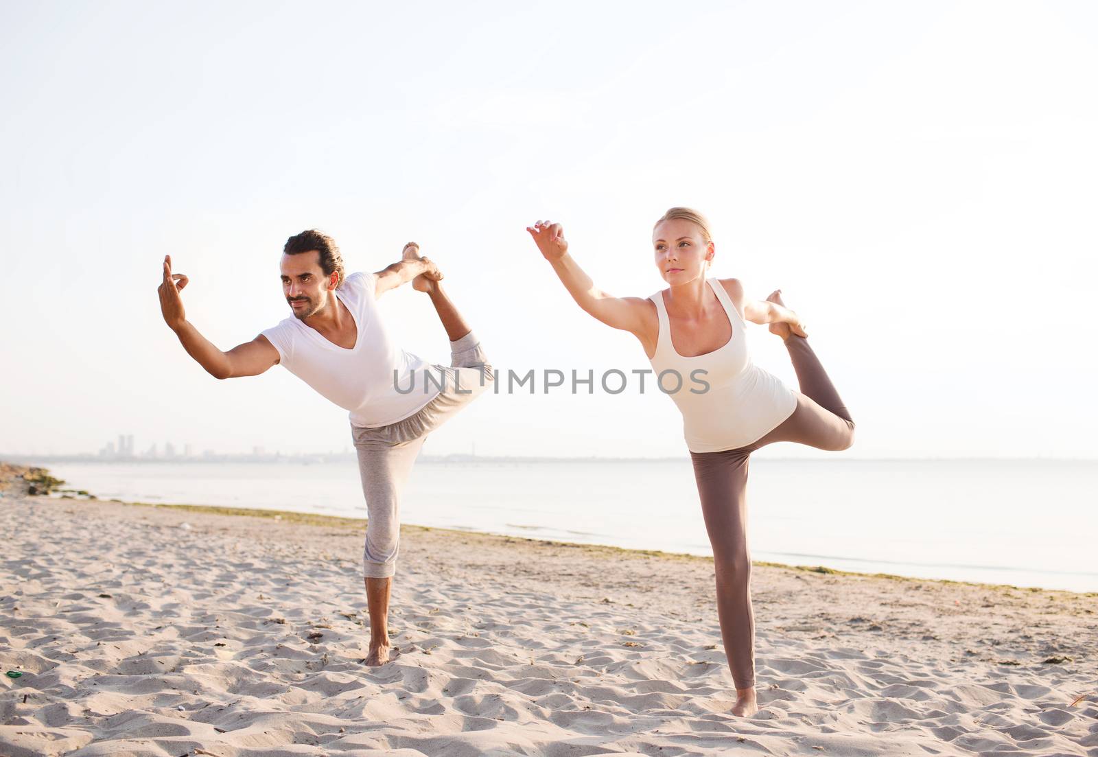 fitness, sport, friendship and lifestyle concept - couple making yoga exercises on beach