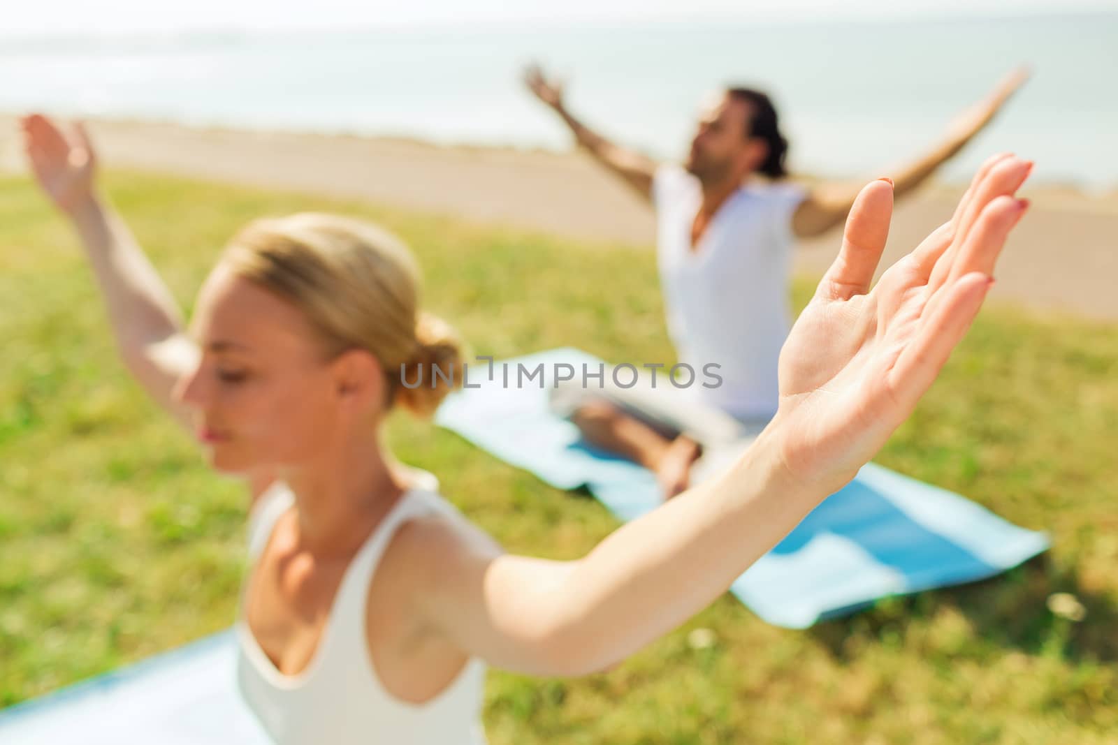 fitness, sport, people and lifestyle concept - close up of couple making yoga exercises sitting with closed eyes on mats outdoors
