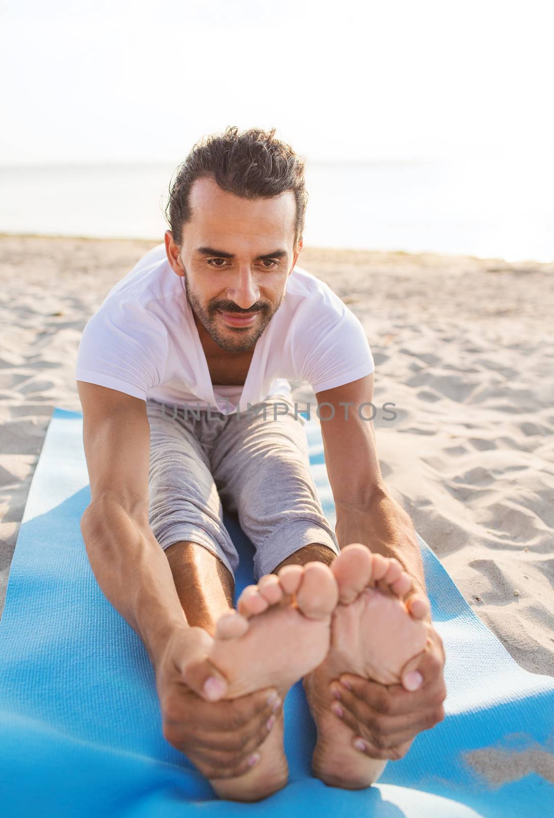 fitness, sport, people and lifestyle concept - man doing yoga exercises sitting on mat outdoors