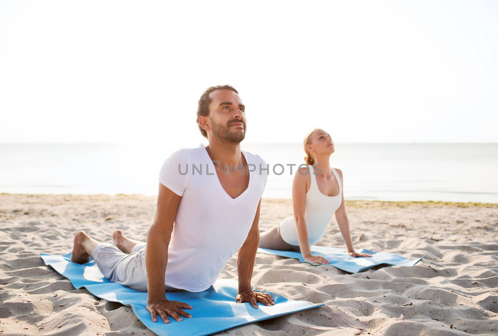 fitness, sport, friendship and lifestyle concept - couple making yoga exercises lying on mats outdoors