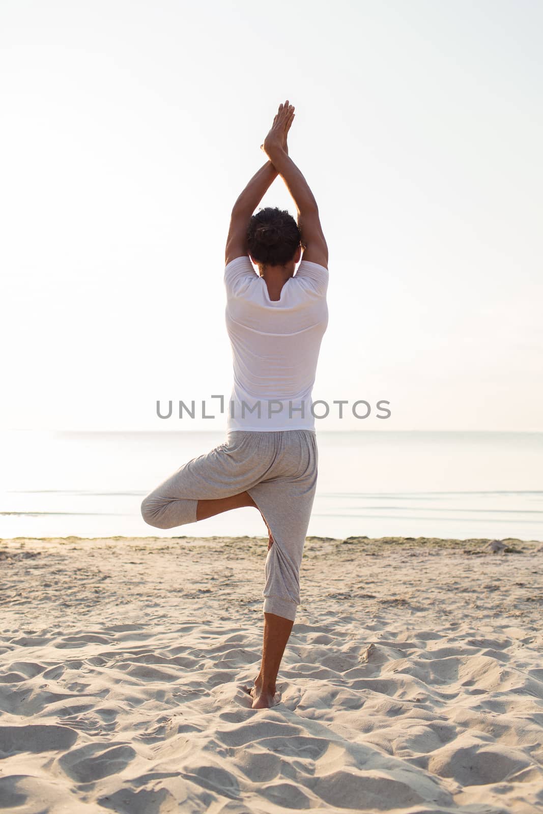 man making yoga exercises outdoors from back by dolgachov