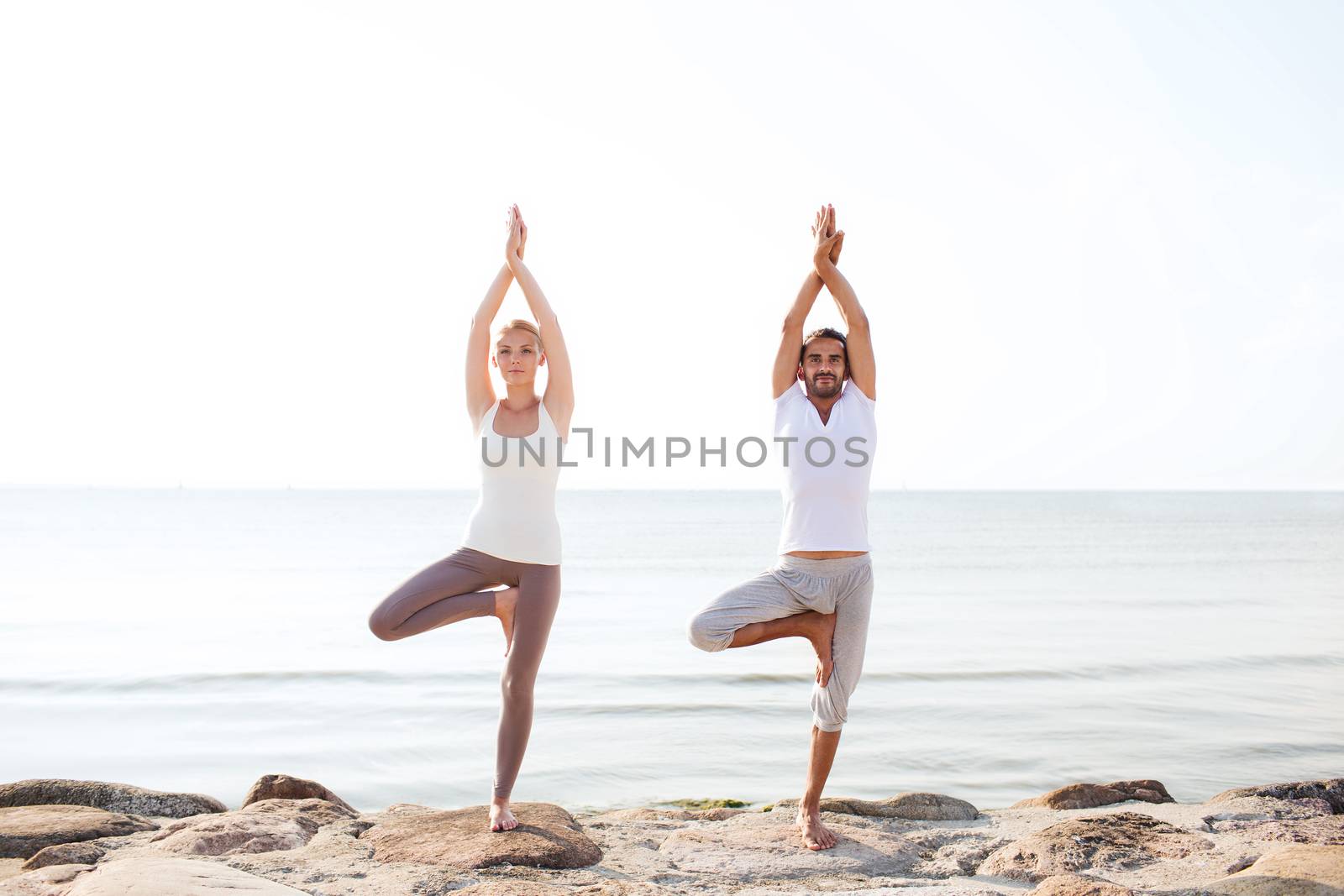 fitness, sport, friendship and lifestyle concept - couple making yoga exercises on beach