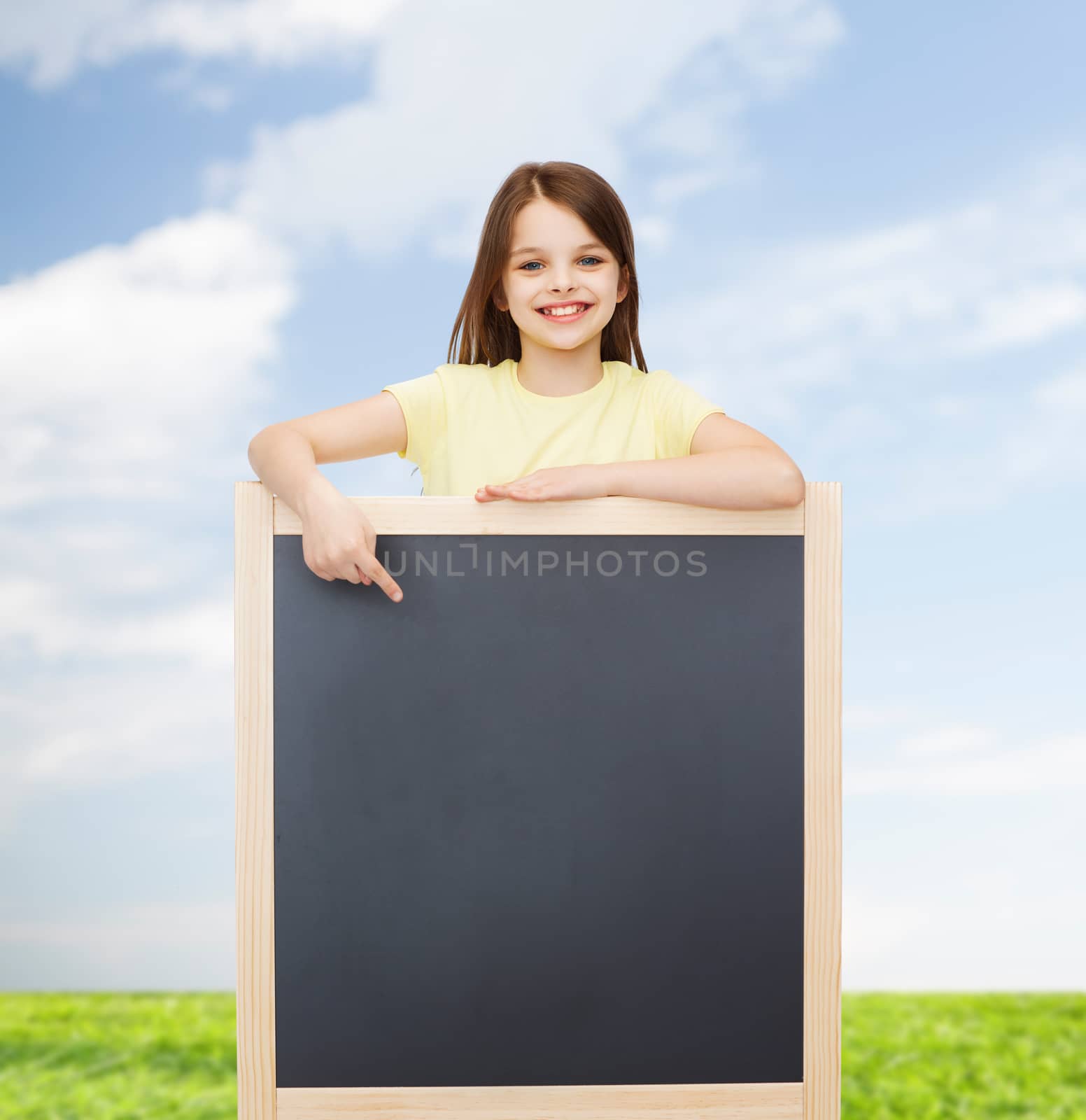 people, advertisement and education concept - happy little girl pointing finger to blackboard