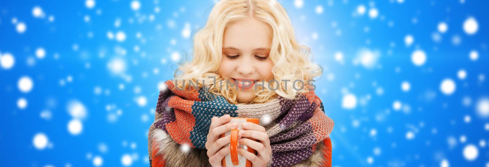 happiness, winter holidays, christmas, beverages and people concept - smiling young woman in warm clothes with cup over blue snowy background