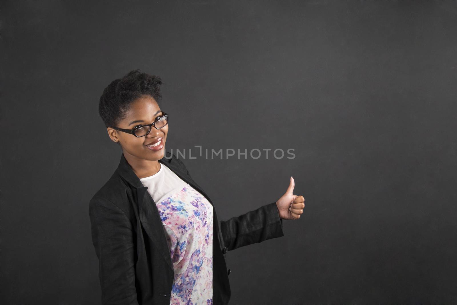 African woman with thumbs up hand signal on blackboard background by alistaircotton
