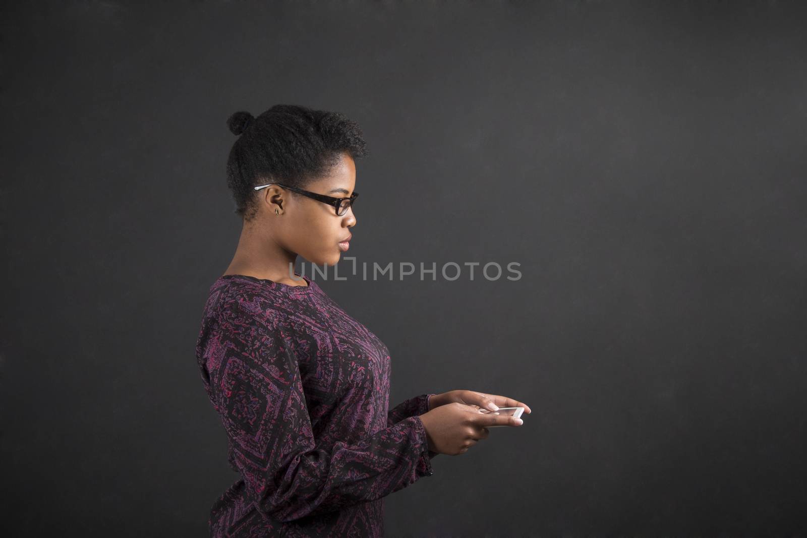 South African or African American black woman teacher or student holding a tablet standing against a chalk blackboard background inside