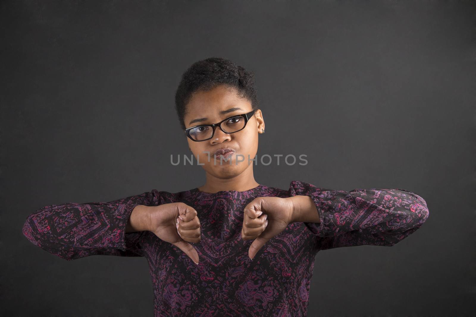 South African or African American black woman teacher or student with thumbs down hand signal on a chalk black board background inside