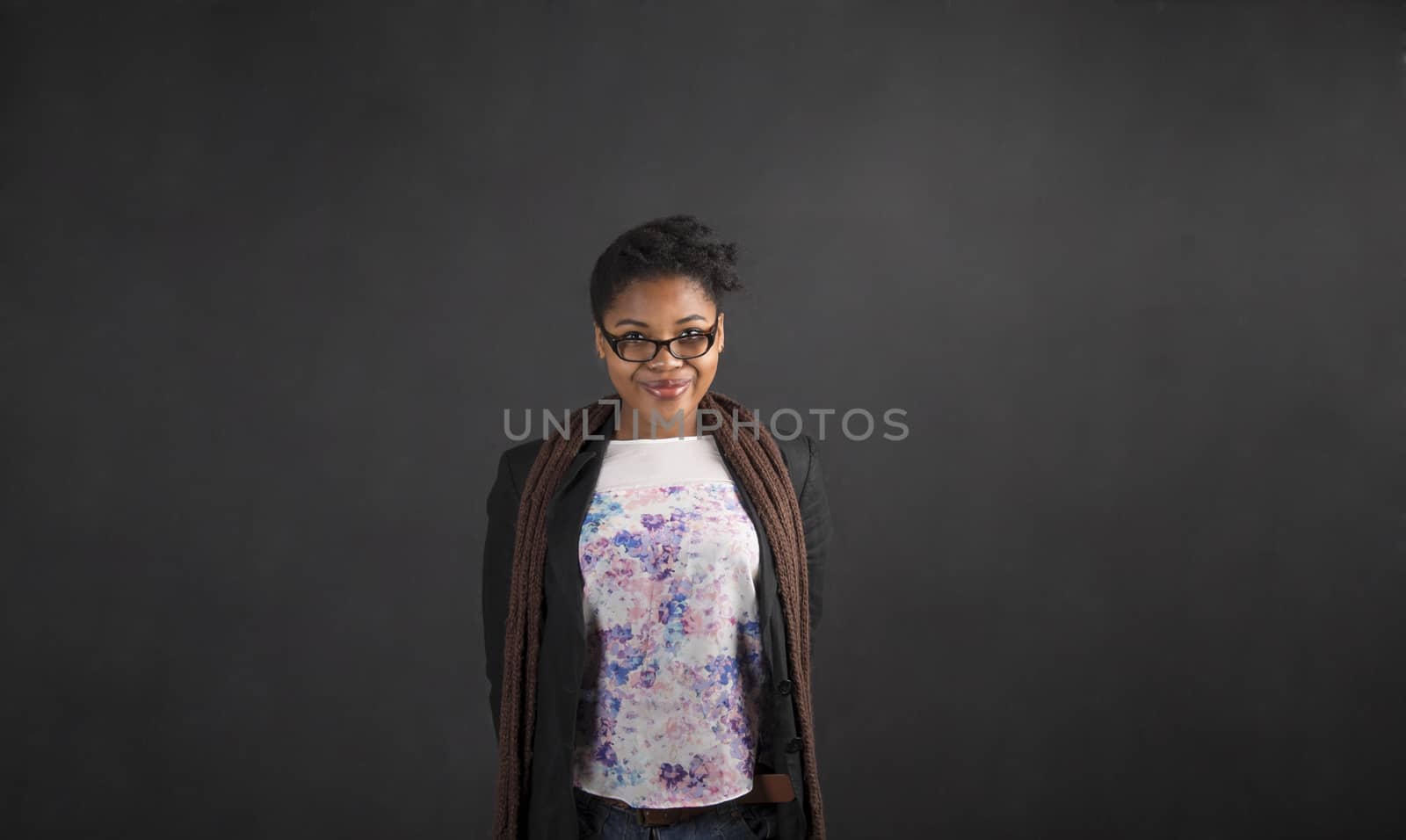 South African or African American black woman teacher or student with her arms behind her back on chalk black board background inside