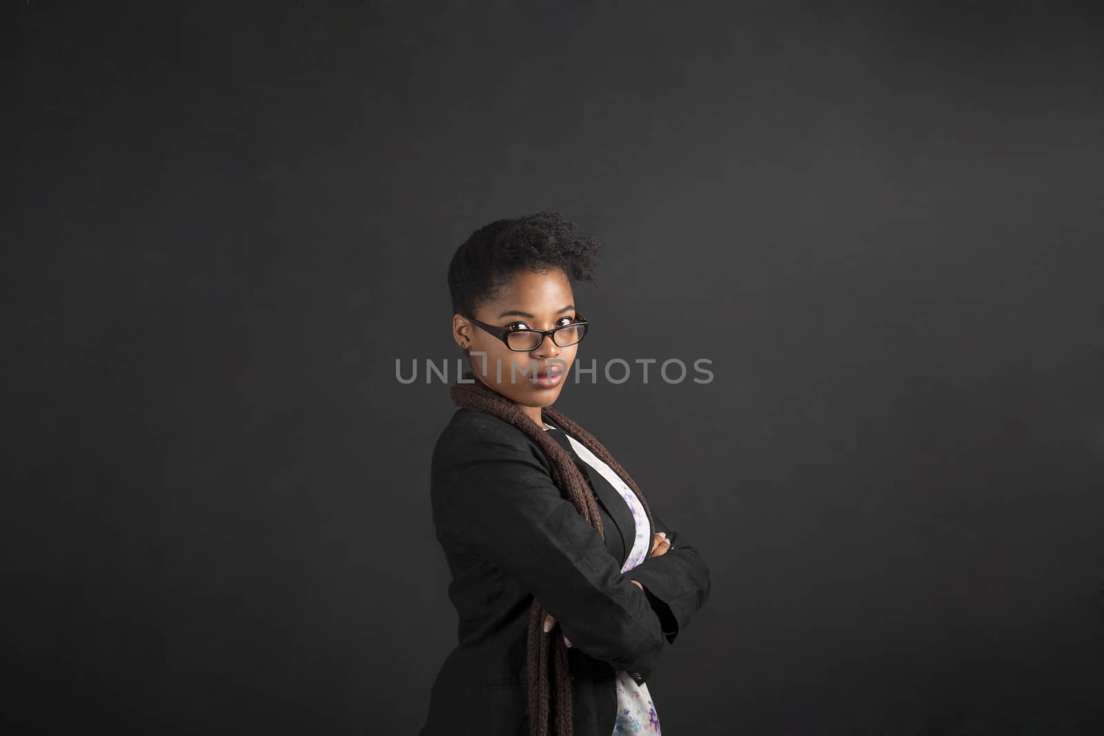 South African or African American woman teacher or student with arms folded on chalk black board background by alistaircotton