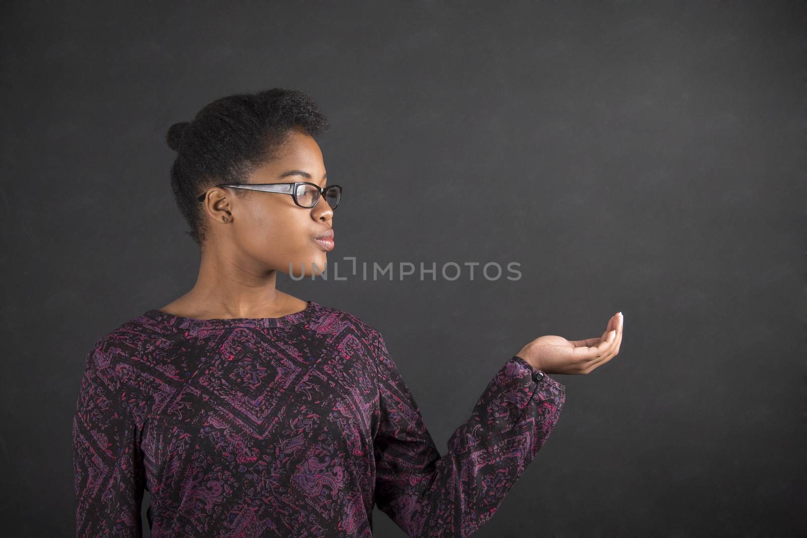 South African or African American black woman teacher or student holding her hand out to the side standing against a chalk blackboard background inside