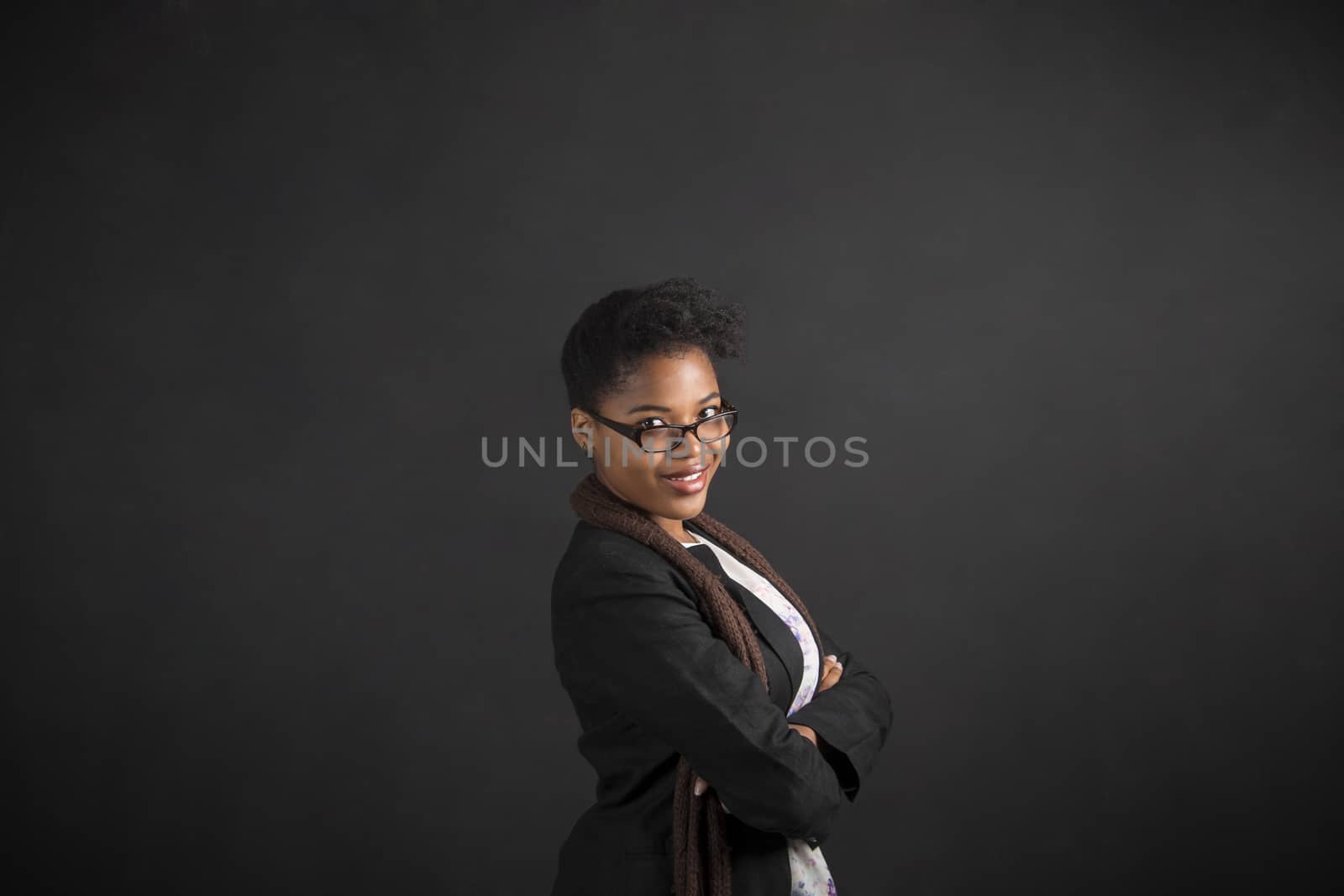 South African or African American woman teacher or student with arms folded on chalk black board background by alistaircotton