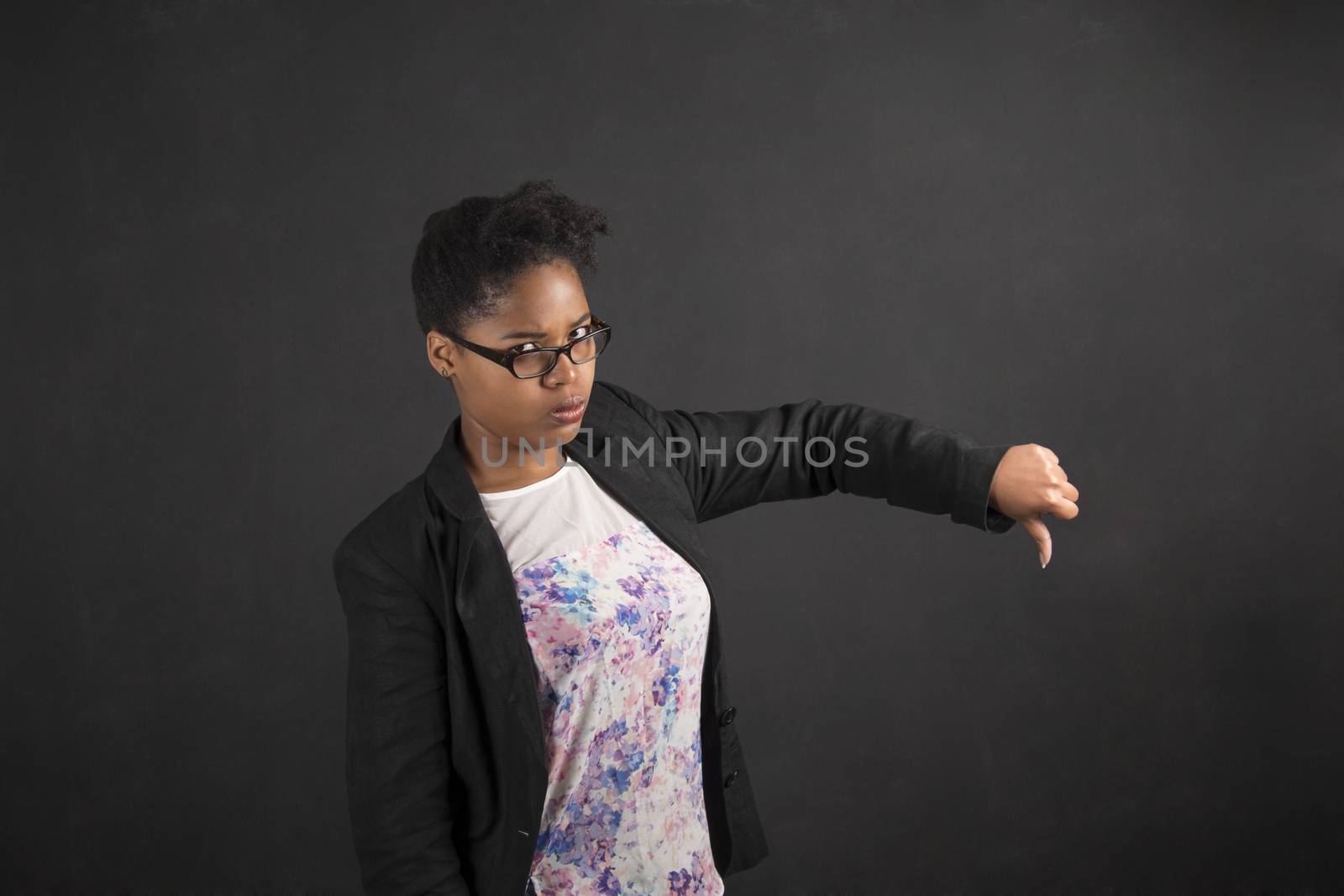 African woman with thumbs down hand signal on blackboard background by alistaircotton
