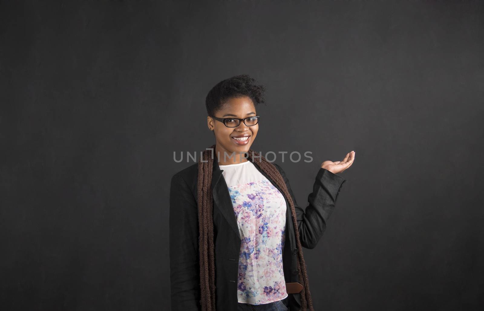 South African or African American black woman teacher or student holding her hand out to the side standing against a chalk blackboard background inside