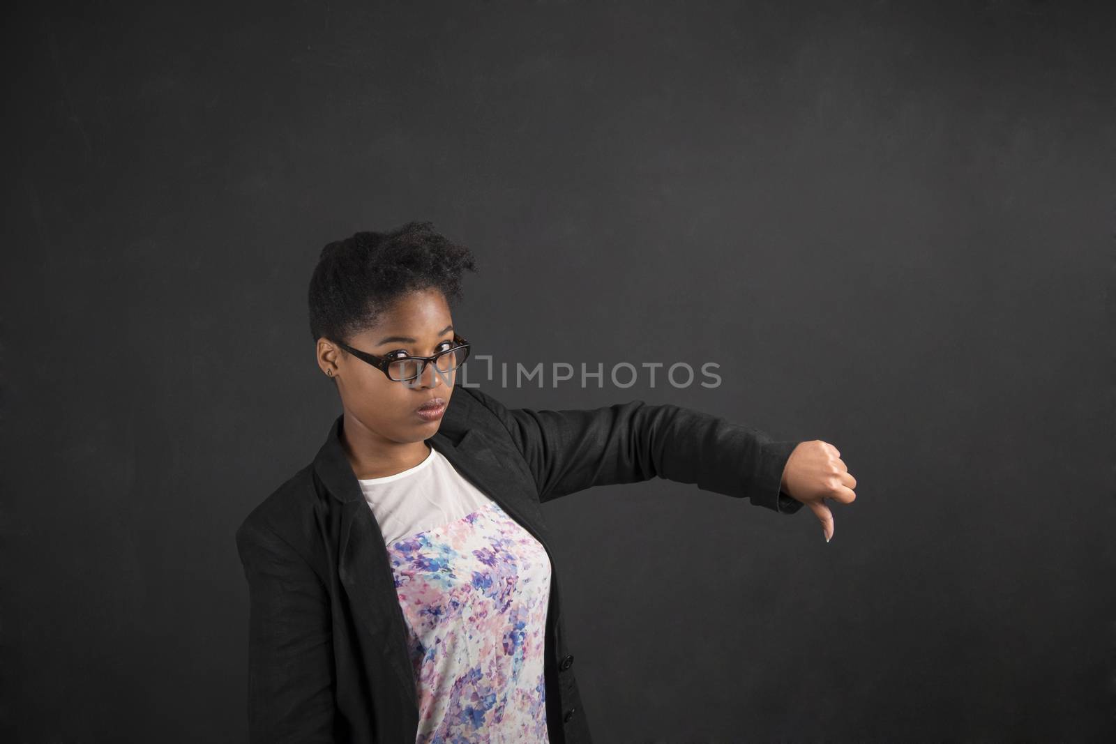 South African or African American black woman teacher or student with thumbs down hand signal on a chalk black board background inside